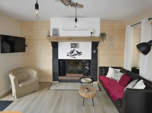Ein Wohnzimmer mit Kamin, einer Couch, einem Sessel, einem Couchtisch und einem an der Wand befestigten Fernseher.