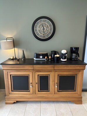 Ein Holzschrank mit einer darüber befindlichen Uhr, eine Lampe, ein Toaster, eine Kaffeemaschine und ein Wasserkocher.