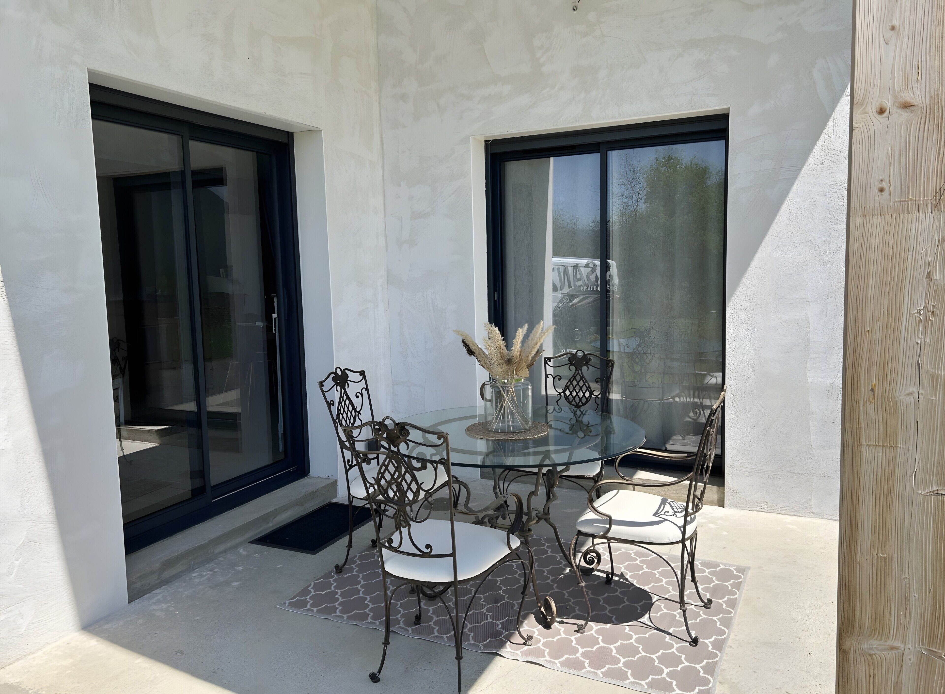 Une terrasse extérieure avec une table en verre, des chaises en métal et un vase contenant des fleurs séchées.