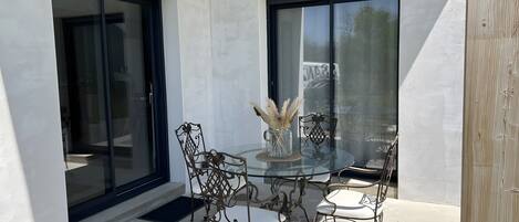Une terrasse extérieure avec une table en verre, des chaises en métal et un vase contenant des fleurs séchées.