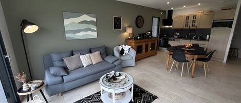 A modern living room with a grey sofa, a coffee table, and a dining area with a black table and chairs.