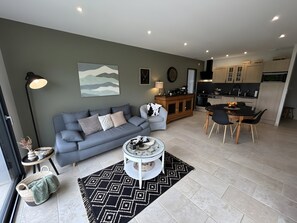 Ein modernes Wohnzimmer mit einem grauen Sofa, einem Couchtisch und einem Essbereich mit einem schwarzen Tisch und Stühlen.