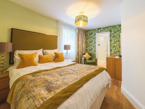 Ein Hotelzimmer mit einem großen Bett, einem Nachttisch, einer Lampe, einem Sessel, einem Schreibtisch und einer Tür.