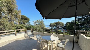 Un patio con una mesa, sillas, una sombrilla y vista al mar.
