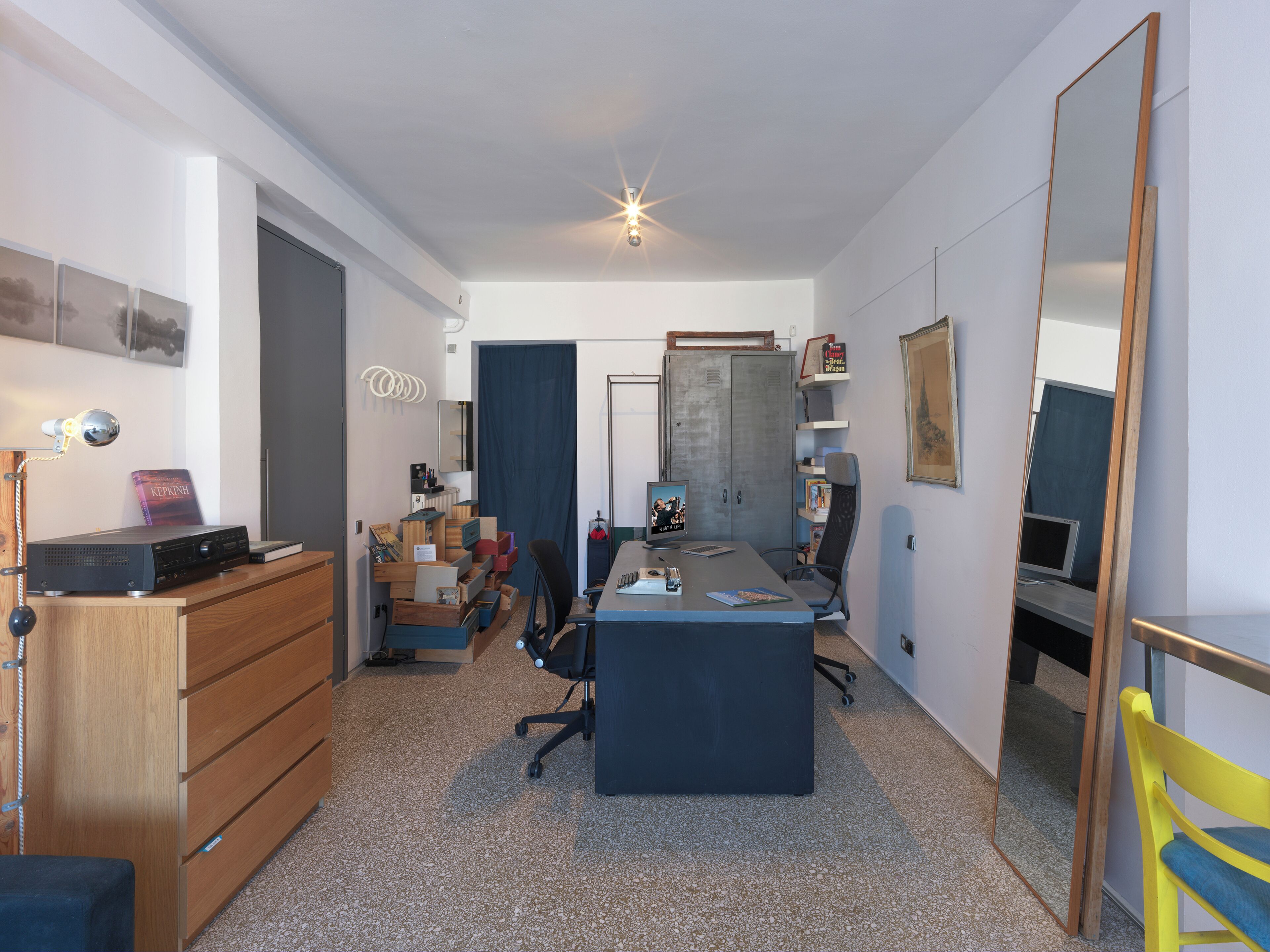 Ein Zimmer mit Schreibtisch, Stuhl, Kleiderschrank und einem großen Spiegel.