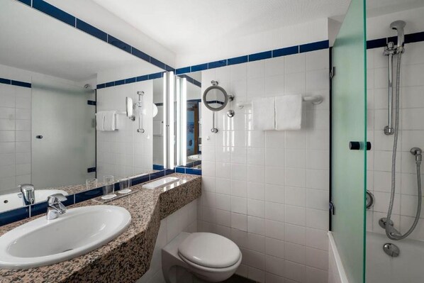 A bathroom with a sink, toilet, mirror, and shower.
