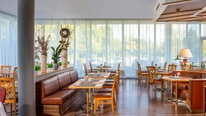 A spacious dining area with multiple tables and chairs, a central sofa, and large windows with sheer curtains.