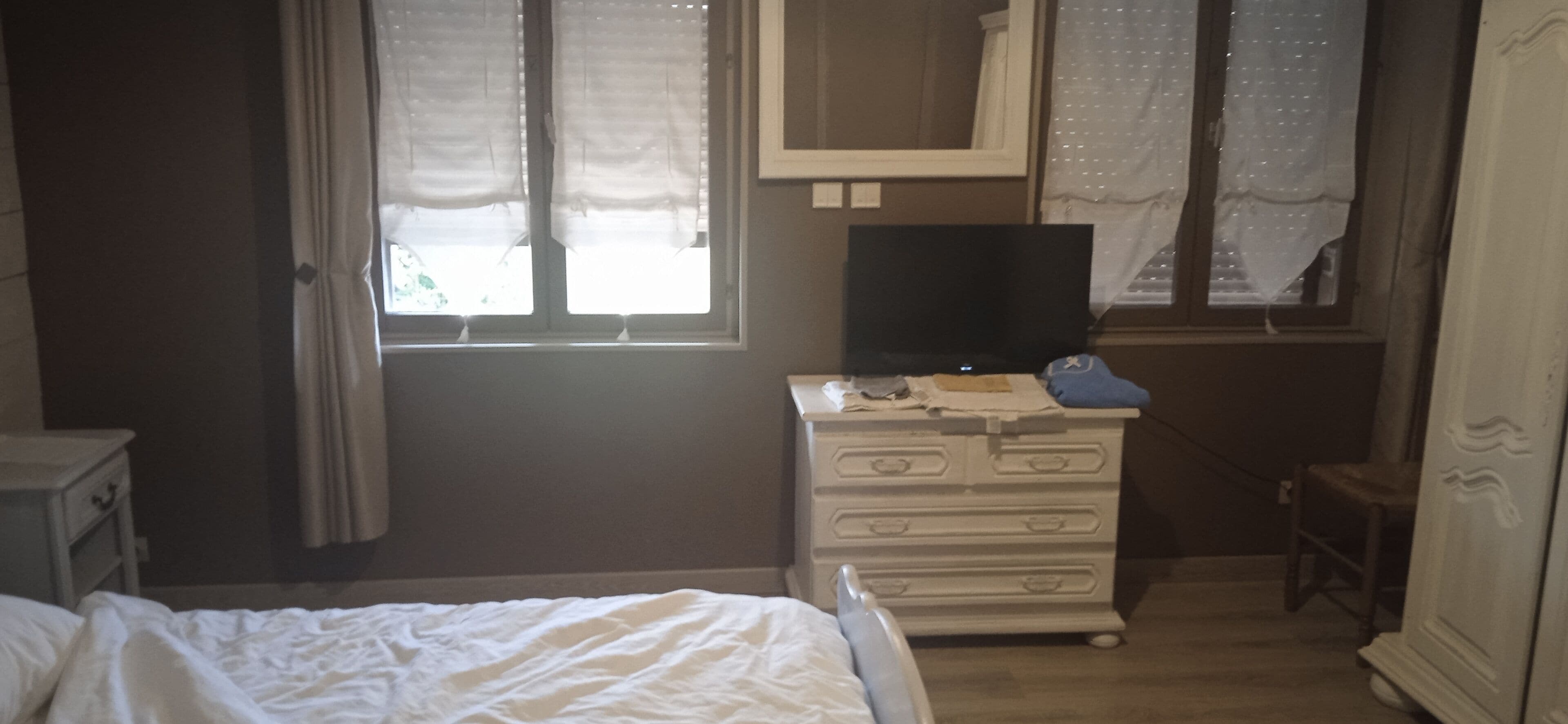 A bedroom with a bed, a dresser, a television on top, and a window with curtains.