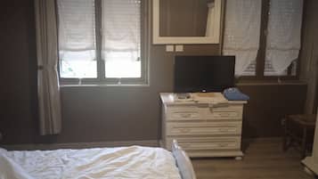 Une chambre à coucher avec un lit, une commode, un téléviseur posé sur le dessus et une fenêtre avec des rideaux.