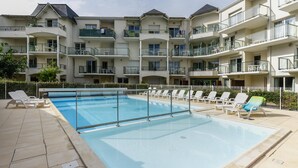 A swimming pool with lounge chairs, a multi-story building with balconies, and a clear sky. - Family Apartment Near Marina (Les Sables-d'Olonne)