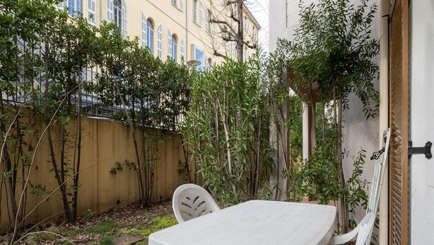 A white plastic table and chairs in a courtyard with a yellow wall, some greenery, and a building in the background. - Apartment in Grasse Near Restaurants (Grasse)