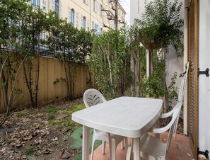 A white plastic table and chairs in a courtyard with a yellow wall, some greenery, and a building in the background. - Apartment in Grasse Near Restaurants (Grasse)