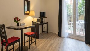 A room with a dining table, chairs, a TV, a lamp, and a window with a view of greenery. - Apartment in Grasse Near Restaurants (Grasse)