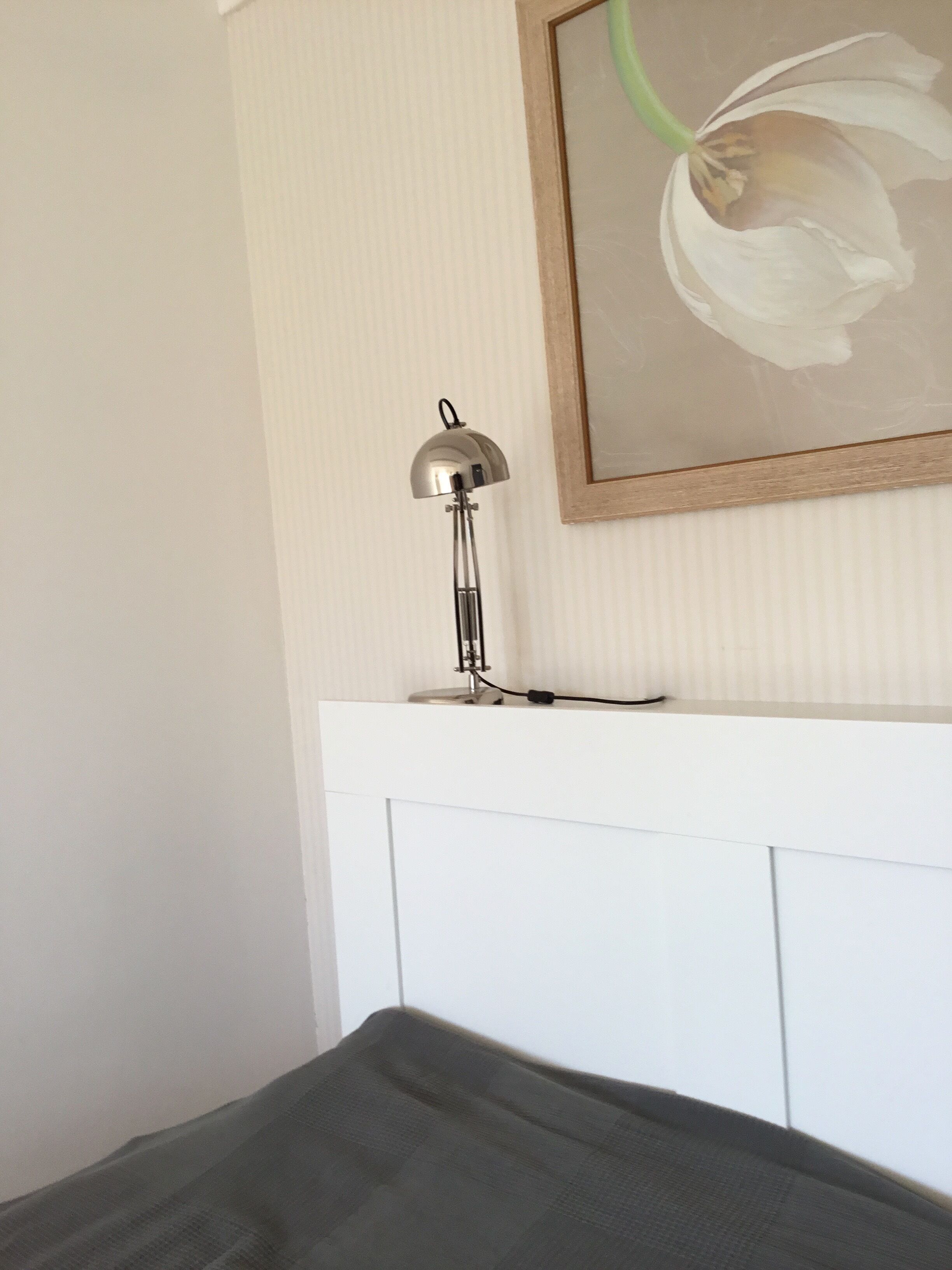 A room with a white headboard, a floor lamp, and a framed picture of a flower on the wall.