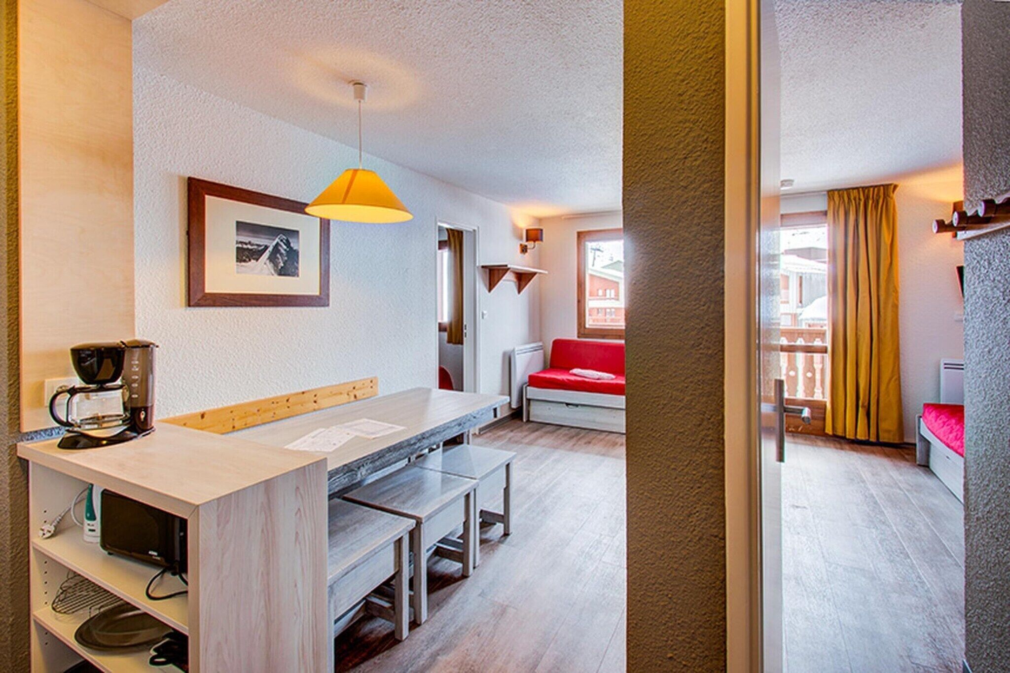 Eine moderne Küche mit Kaffeemaschine, Esstisch und Bänken. Im Hintergrund steht ein rotes Sofa und ein Fenster mit Vorhängen.