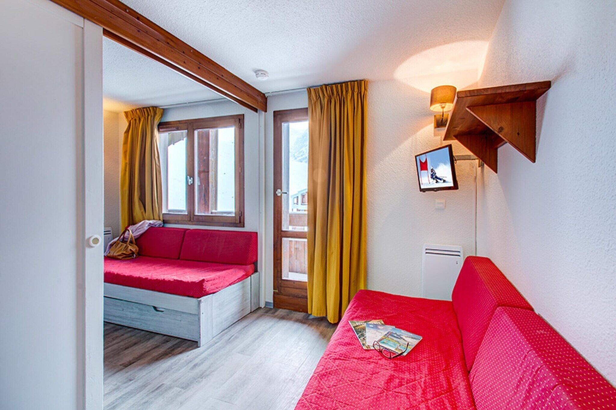 Ein Zimmer mit einem roten Sofa, einem Fenster mit gelben Vorhängen, einer Holzbalkendecke und einer Wandleuchte.