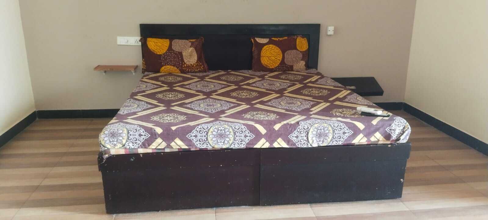 A bed with a patterned bedspread, a headboard, and a bedside table with a lamp.