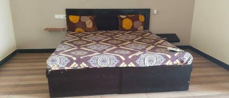 A bed with a patterned bedspread, a headboard, and a bedside table with a lamp.