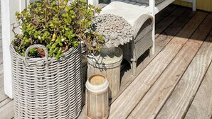 Un espacio al aire libre techado con una banca y sillas, una maceta de mimbre y una mesita.