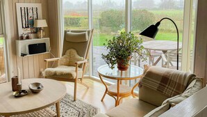 Una habitación acogedora con sofá, una mesa redonda, una silla, una lámpara, una planta en maceta y vistas al exterior.