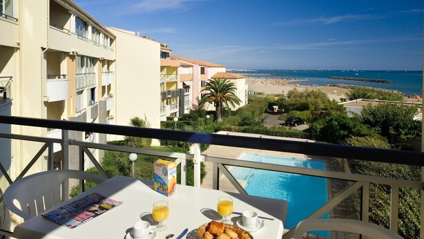 Un balcone con un tavolo apparecchiato per la colazione, vista su una piscina e una spiaggia.