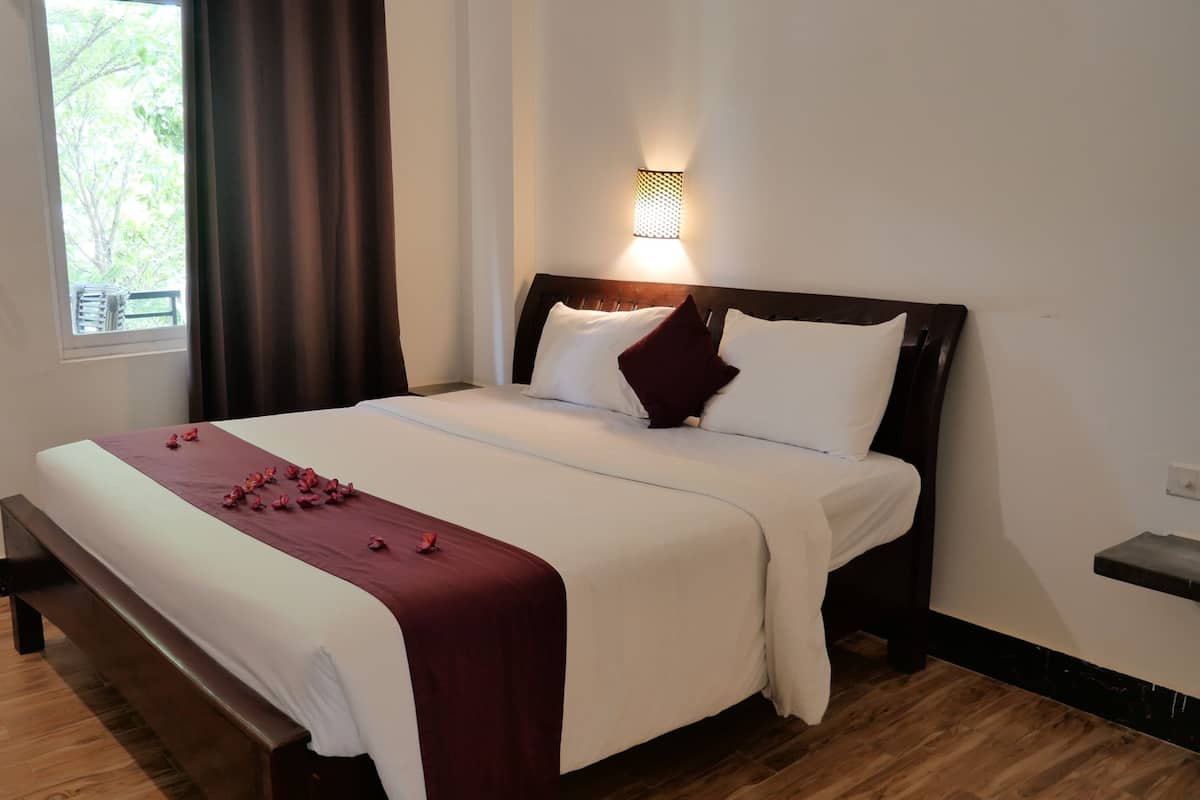 A neatly made bed with a white and maroon bedspread, a wooden headboard, and a wall-mounted light fixture.