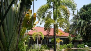 A tropical resort with a red-roofed building, a curved pathway, and a pond. - STC Hotel School (Siem Reap)