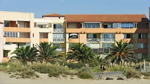 Un hotel de varios pisos con balcones, palmeras y un primer plano de arena.