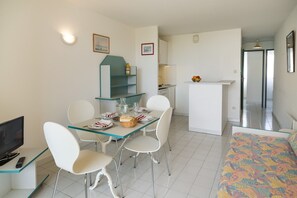 Ein gemütlicher Raum mit Esstisch, Stühlen, Fernseher, Bett und Küchenzeile.