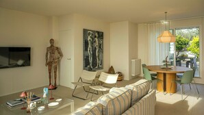 A modern living room with a sofa, chairs, a dining table, a TV, and artwork.