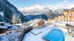 A hotel with a pool, snow-covered surroundings, and mountains in the background. - Alpine Comfort Apartment Near Ski-slopes (Modane)
