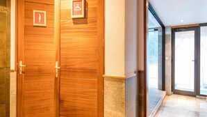 A wooden double door with a coat of arms and a hanger symbol, leading to a tiled interior. - Alpine Comfort Apartment Near Ski-slopes (Modane)