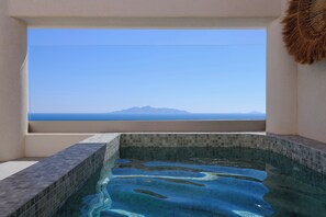 Vista despejada de una piscina con borde de azulejos y ventana con vistas a una montaña y al mar a lo lejos.