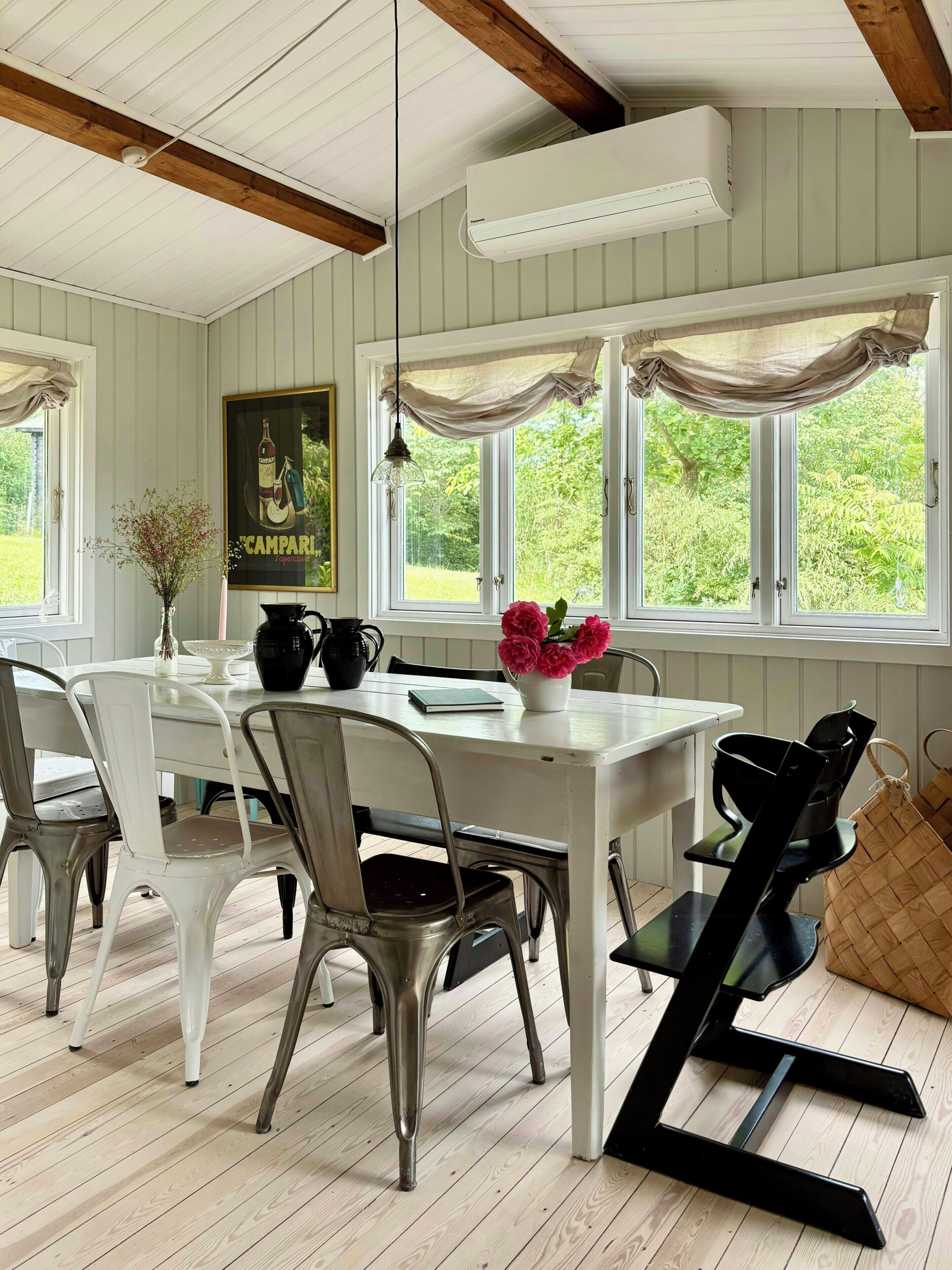 Et spiseområde med et hvidt bord, metalstole og et vindue med gardiner.