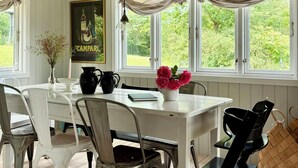 Un comedor con una mesa blanca, sillas metálicas y un ventanal con cortinas.
