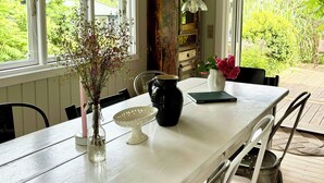 Un comedor con una mesa, sillas, un jarrón con flores, una jarra y un libro.