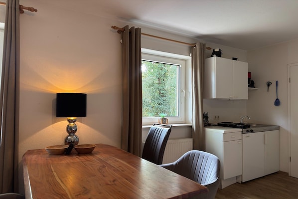 Cocina compacta con comedor, ventana con cortinas, una planta pequeña y una lámpara.