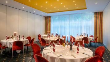 A conference room with multiple round tables, red chairs, and a large window with curtains.