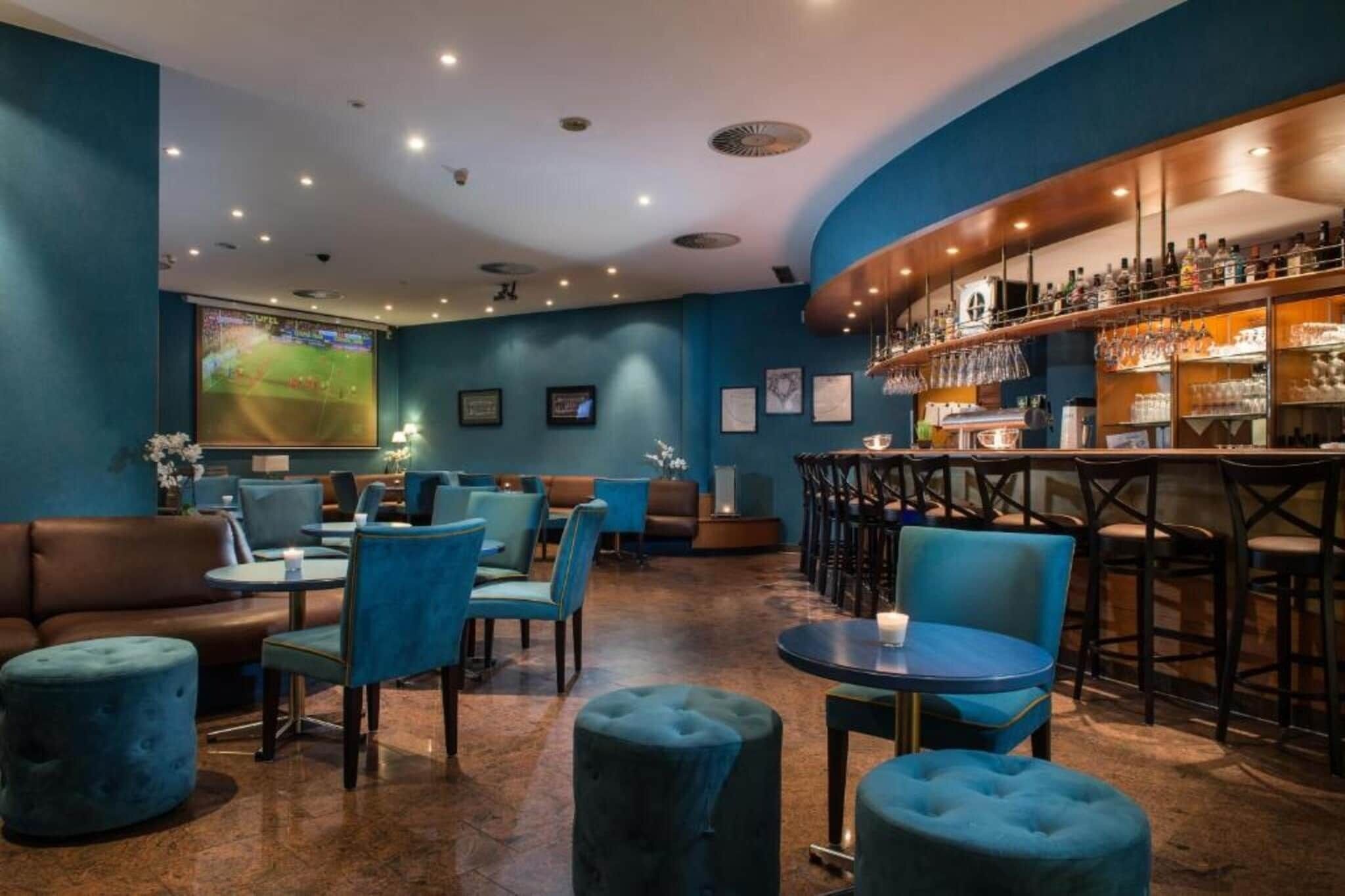 Zona de bar con asientos, una pantalla de televisión y una barra llena de botellas.