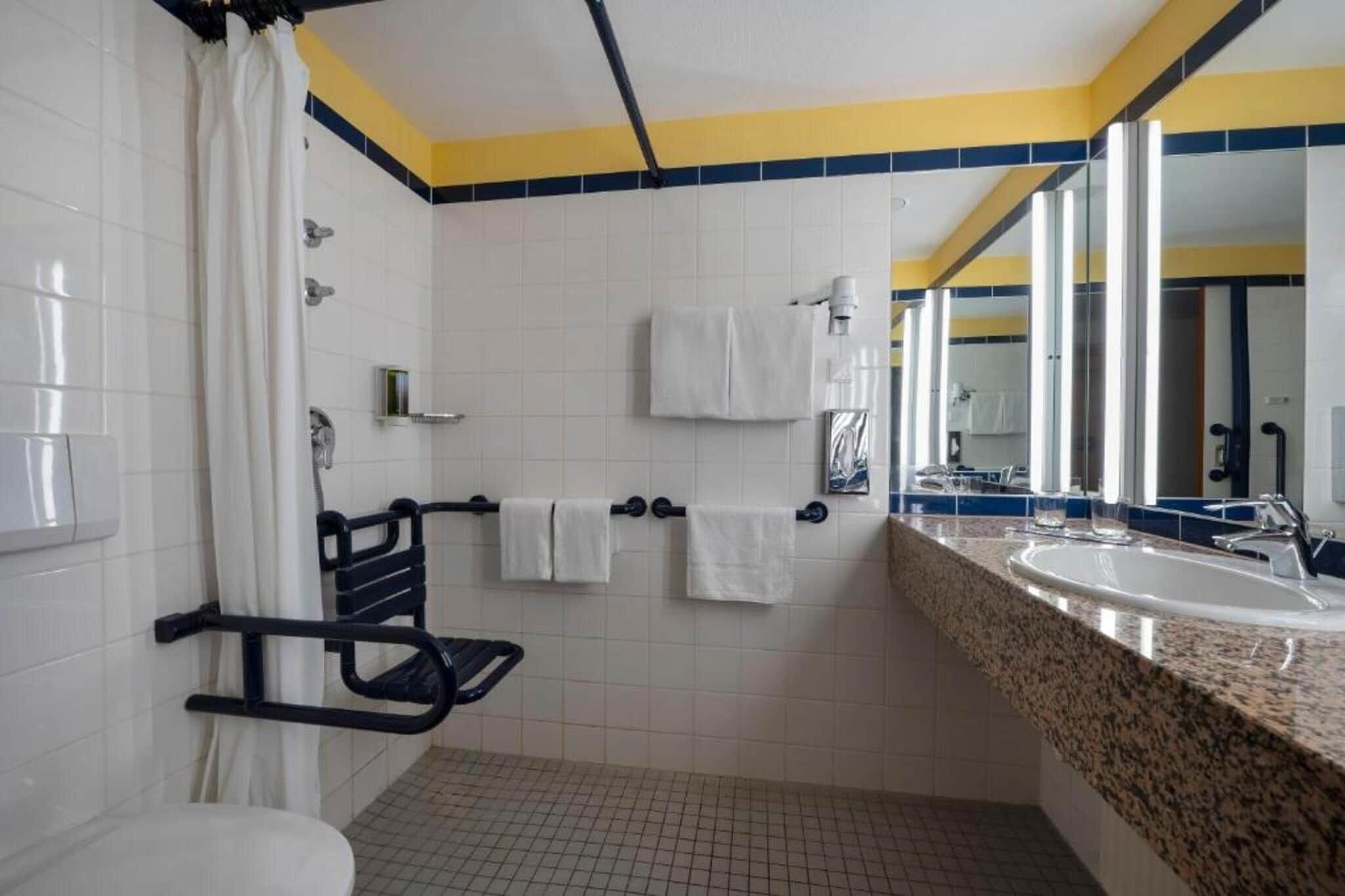A bathroom with a white toilet, a shower with a curtain, a sink with a mirror, and a towel rack with multiple towels.