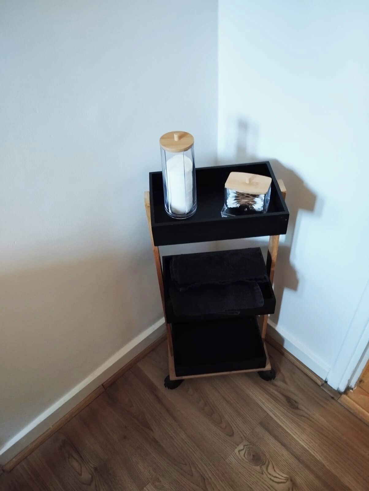 Esquina de una habitación con un mueble negro de madera que sostiene una vela blanca y una caja.