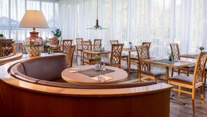 A hotel lobby with a round seating area, wooden tables, and chairs, a lamp, and sheer curtains. - Sunday Hotel Spa Wismar Disability access (Wismar)
