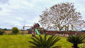 A playground with a slide and swings, surrounded by grass and potted plants. - Charming Air-Conditioned House –Pyrenees Views, Tennis & Large Garden (Sleeps 8) (Uzan)