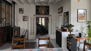 A cozy room with a wooden ceiling, a large clock, a dining table with chairs, a small cabinet, and a potted plant. - Charming Air-Conditioned House –Pyrenees Views, Tennis & Large Garden (Sleeps 8) (Uzan)