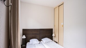 A single bed with a wooden headboard, two bedside tables with lamps, and a closed door. - Functional Alpine Base for 8 Guests (Loudenvielle)