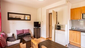 A compact living space with a sofa, a TV, a dining table, and a kitchenette. - Functional Alpine Base for 8 Guests (Loudenvielle)