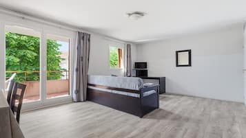 A bedroom with a bed, a TV, and a balcony with curtains.