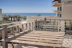 Un balcon donnant sur la mer, avec des palmiers et un immeuble doté d’un balcon.