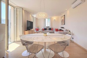 Un salon moderne avec une table en marbre, des chaises en fil de fer, un grand téléviseur et un lustre décoratif.