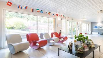 Un área de espera moderna con sillas de colores, una mesa con folletos y un techo con baldosas estampadas.